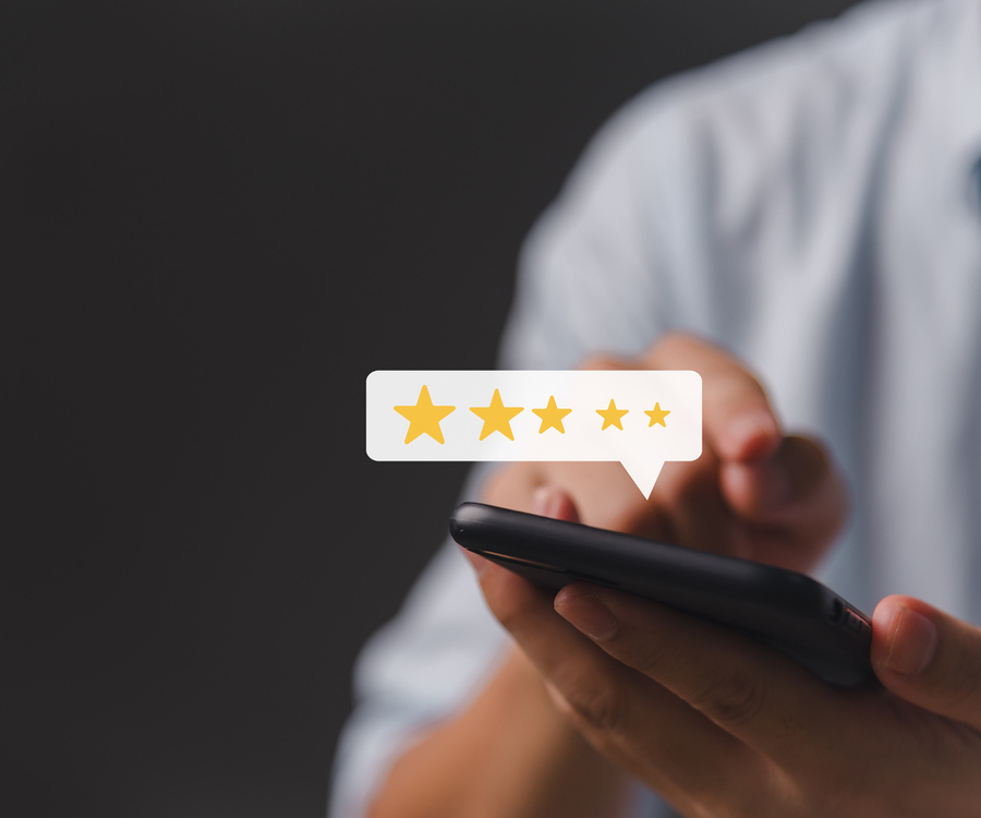 Man in a white shirt holding a smartphone, a five-star rating in a speech bubble floating above the screen against a dark background