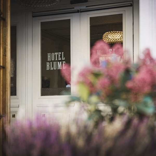 Entrance of BLUME. Baden Hotel & Restaurant with the hotel name on the glass door and pink flowers in front, Baden, Switzerland